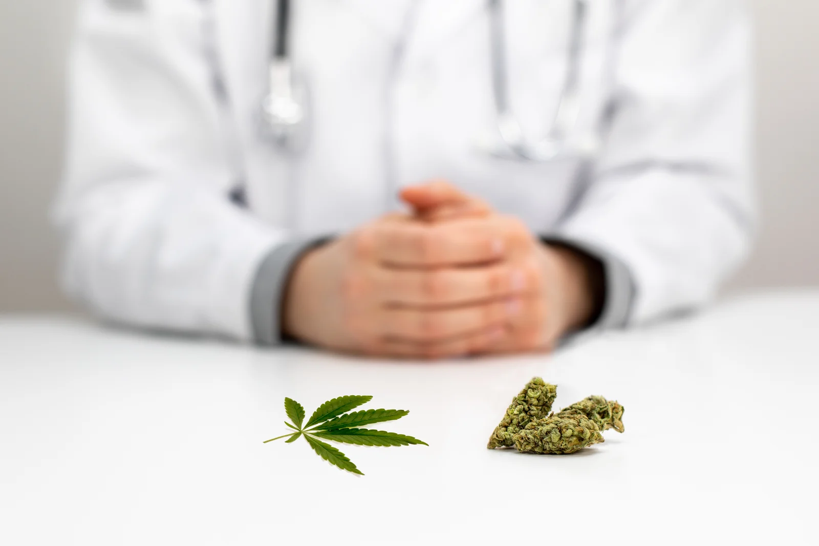 A doctor sitting at a desk with cannabis buds and a leaf displayed in front, symbolizing the study of medical marijuana strains for treatment.
