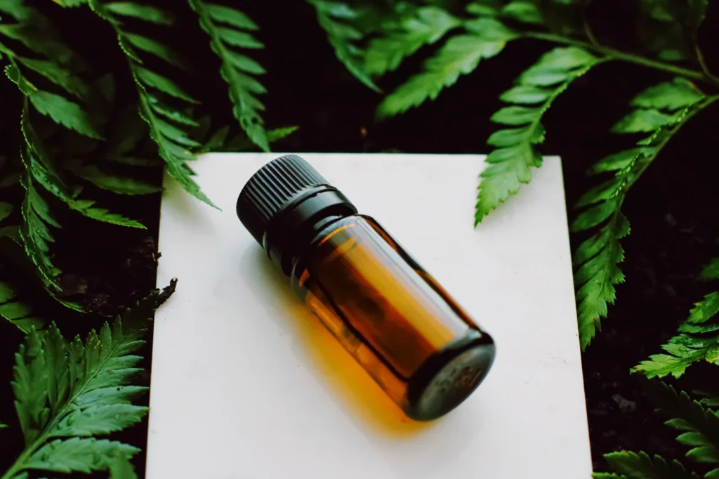Amber glass bottle of cannabis oil surrounded by green leaves, representing natural extracts used in cannabis oil pens and wellness products.