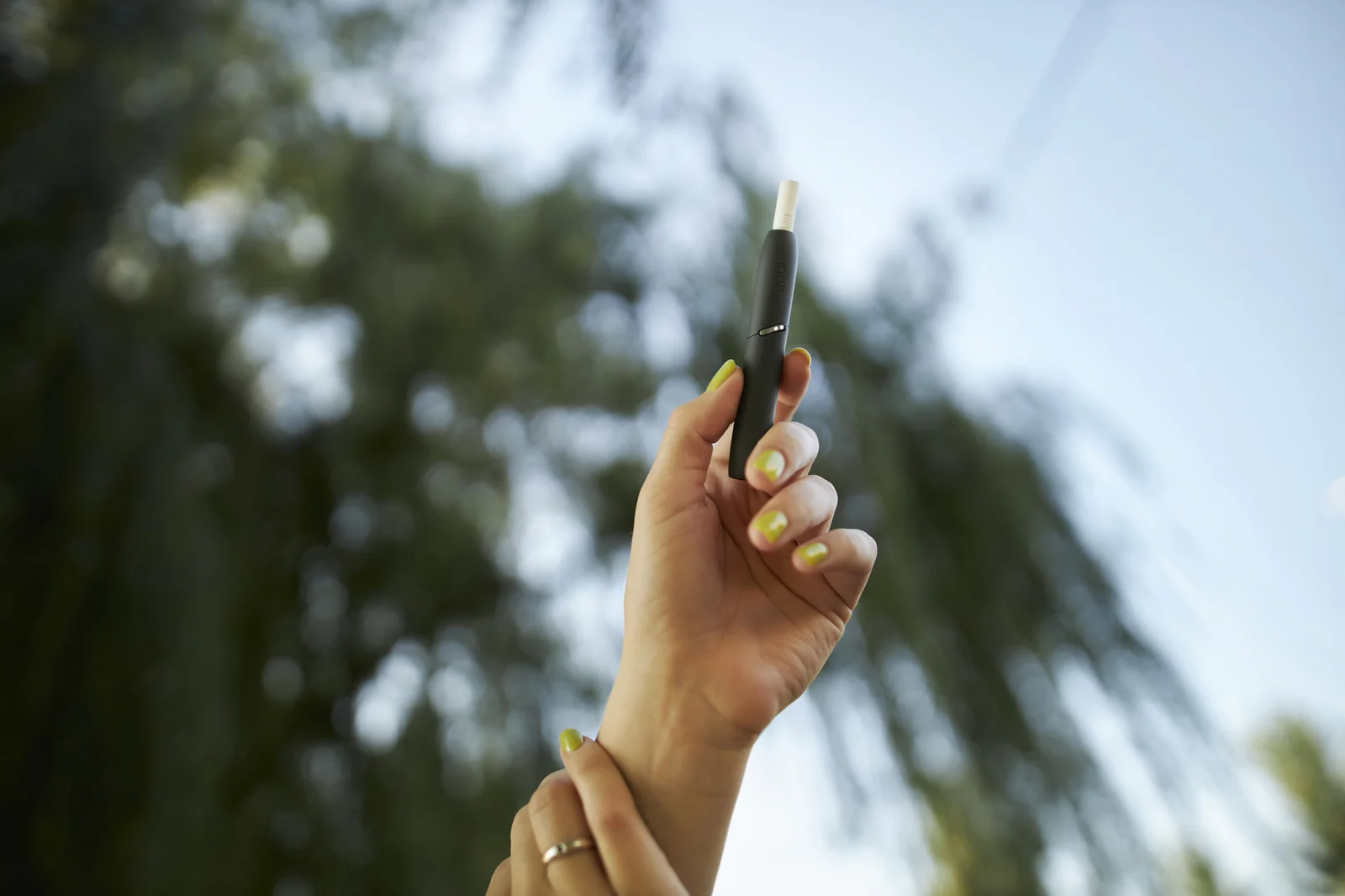 Hand holding a sleek black vaporizer outdoors against a blurred background, showcasing modern cannabis oil pens used for vaping.