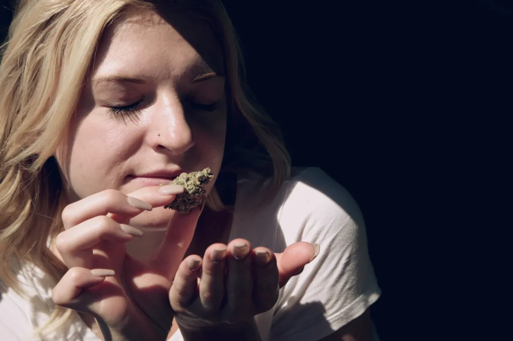 Woman smelling a cannabis bud in natural light, exploring how long does cannabis stay in your system through personal experience.