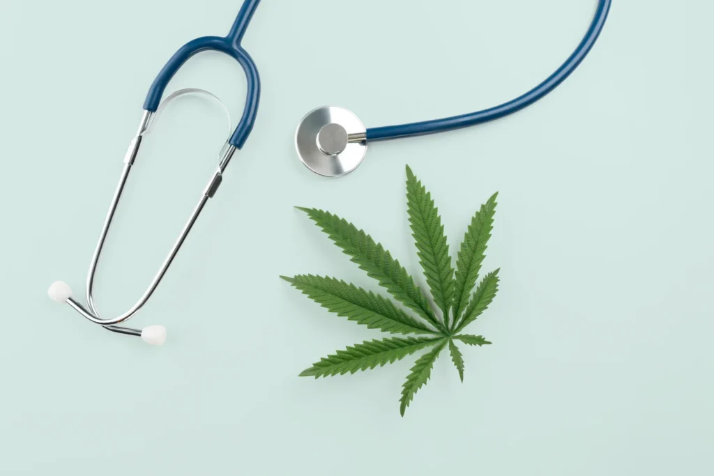 A flat lay of a stethoscope next to a cannabis leaf on a pale green background, highlighting the concept of medical marijuana for insomnia and alternative wellness care.