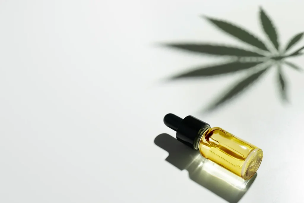 Glass dropper bottle filled with golden cannabis sativa seed oil casting a leaf shadow on a white background