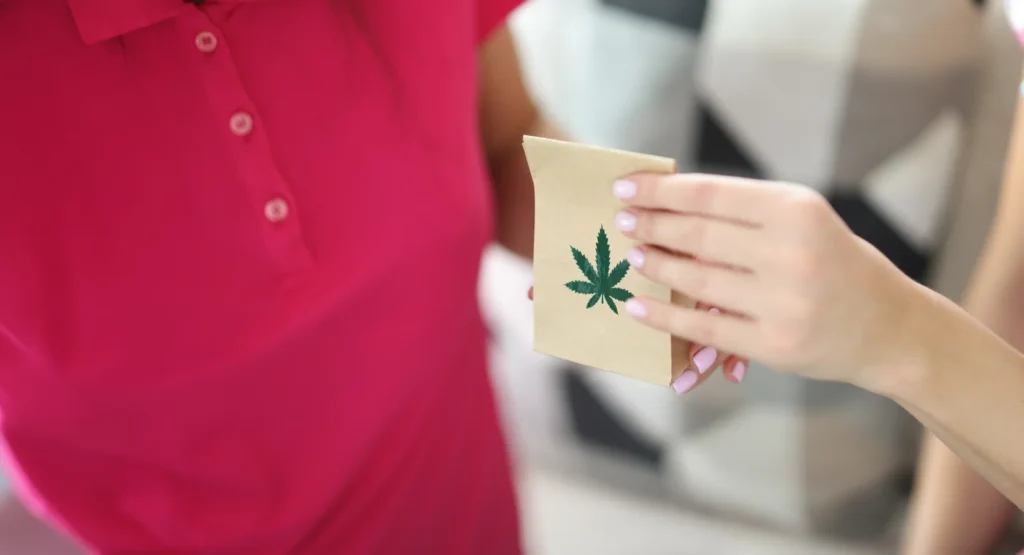 A person handing over a small paper bag labeled with a cannabis leaf, representing convenient purchase and access provided through cannabis card benefits.