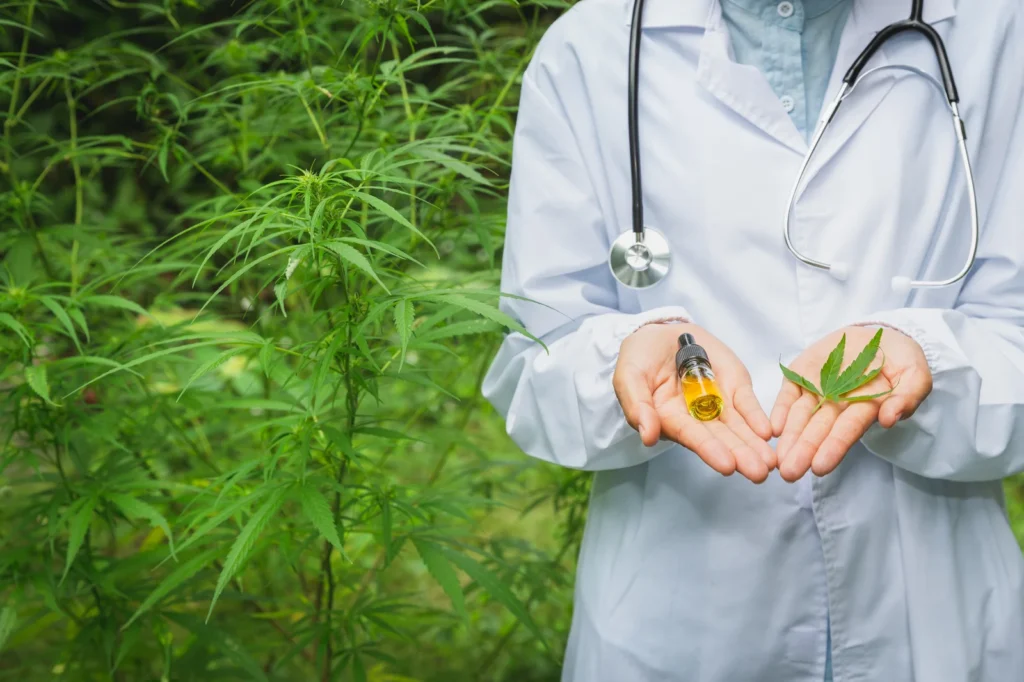 A doctor holding cannabis oil and a marijuana leaf while standing in a hemp garden, illustrating ADHD and Medical Cannabis treatment options.