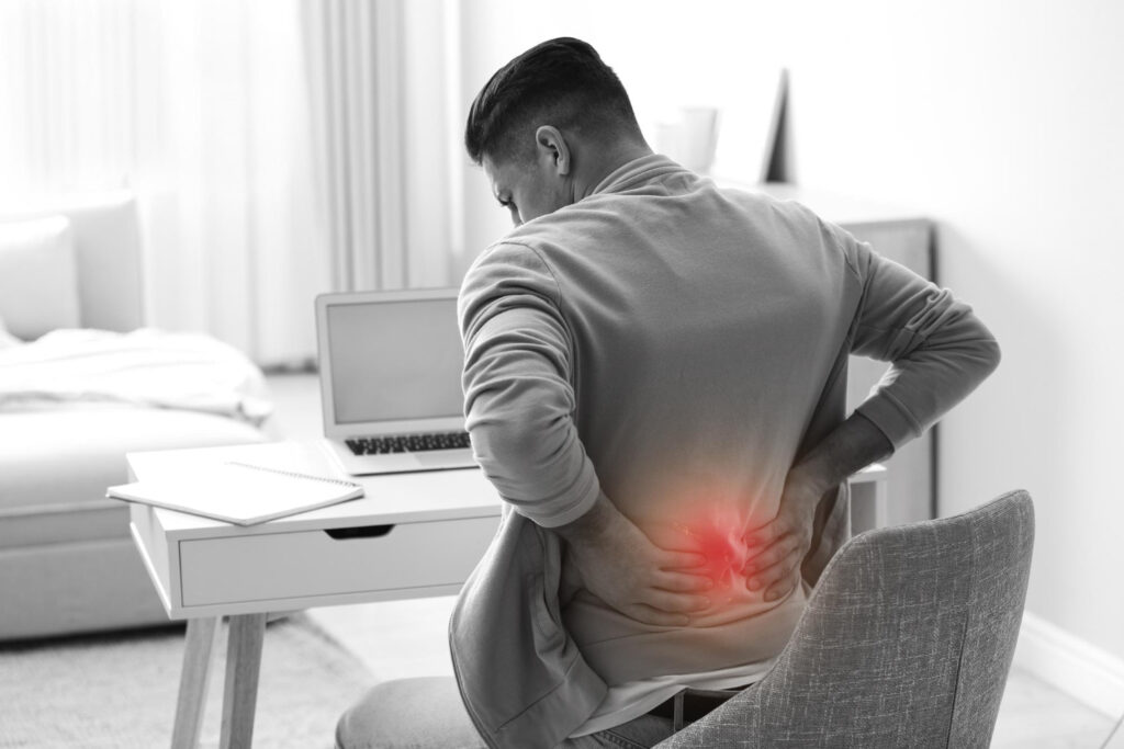 Man holding his lower back in discomfort at a desk, showing medical cannabis for back pain as an alternative approach to chronic pain relief.